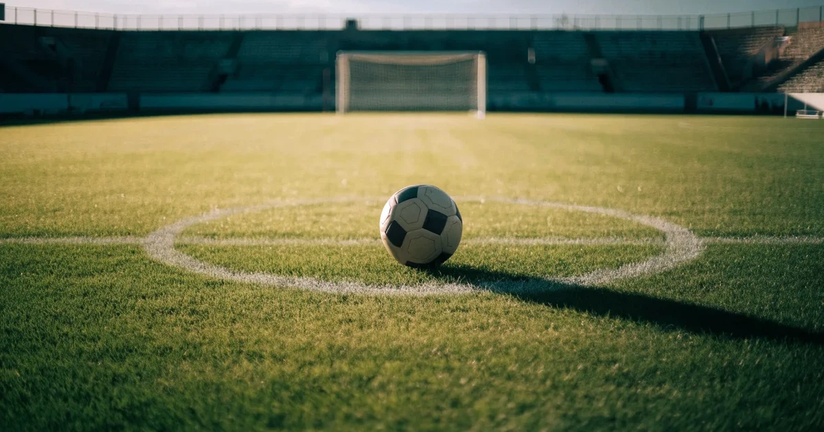 Uma bola de futebol no ponto central de um relvado, à luz da manhã
